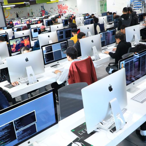 Workroom with students working on iMacs with street art in the background - 1337 Benguerir campus (Morocco)