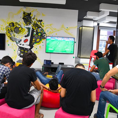 Students sitting on beanbags and watching a soccer game together in a room with street art on the walls - 1337 Khouribga campus (Morocco)